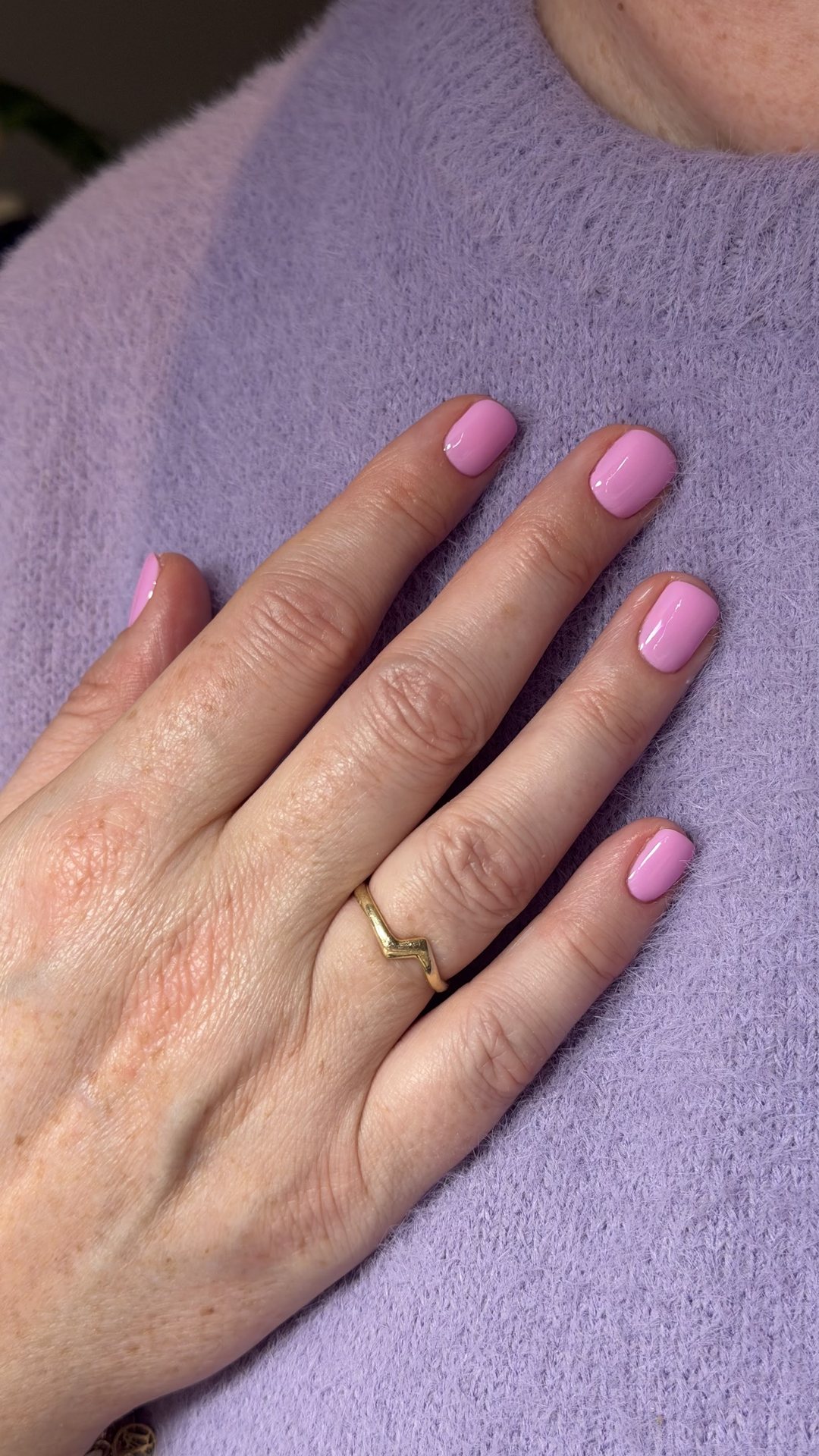 Zachtroze manicure op een lila gebreide trui