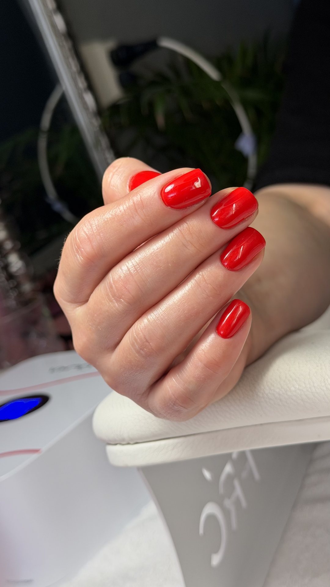 Helderrode manicure op de handsteun, naast de nagellamp